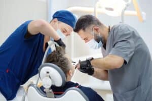 Two dentists examine patient's teeth in modern dental office using professional equipment.