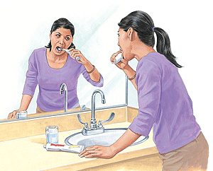 Woman brushing teeth at bathroom sink after dental implant surgery.