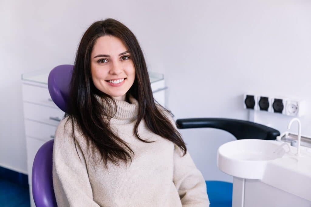 Woman smiling in dental chair at modern dentistry office with purple headrest and equipment.