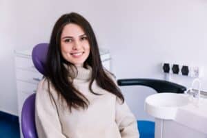 Woman smiling in dental chair at modern dentistry office with purple headrest and equipment.