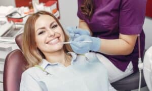 Woman receiving dental examination in dentist's chair with dental professional wearing gloves.