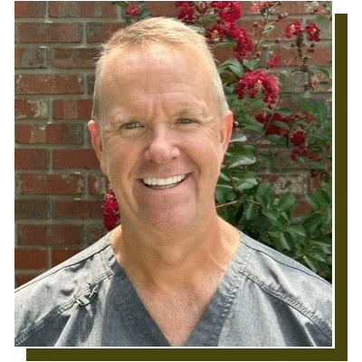 Smiling male dentist in scrubs against brick wall with red flowers