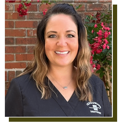 Professional headshot of smiling woman in dental scrubs against brick wall with flowering vines.