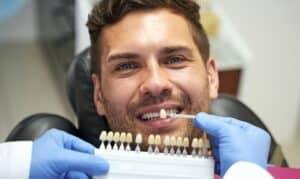 Dentist in blue gloves examines dental implant model in clinical laboratory setting.