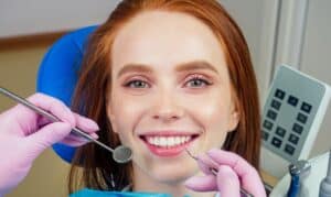Young patient smiling during dental examination with dentist holding tools in clinical setting.