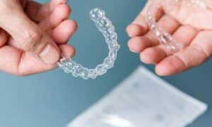 Hands holding clear orthodontic aligners against blue background with storage case below.