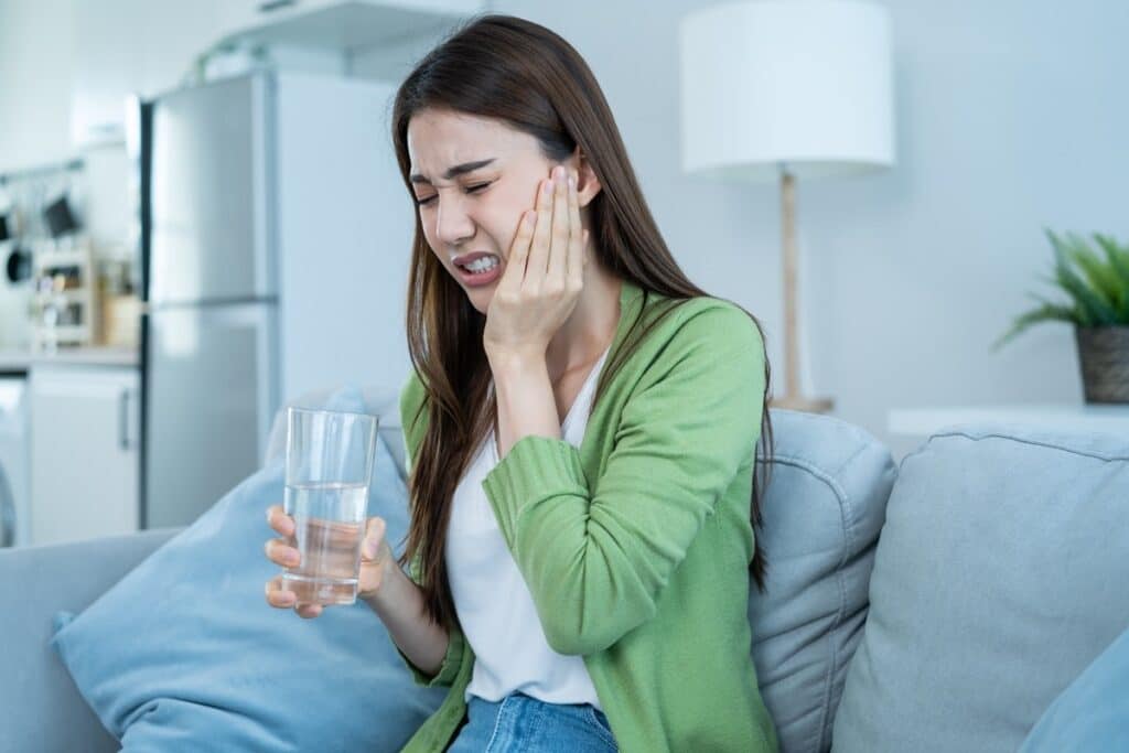 Woman with toothache holding cheek in pain while sitting on couch at home.