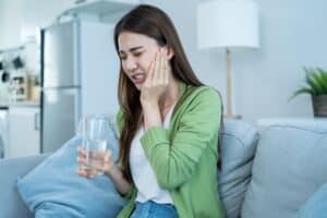 Woman with toothache holding cheek in pain while sitting on couch at home.