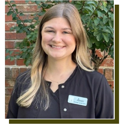 Young woman in dark dental scrubs smiling at camera against brick wall with ivy.