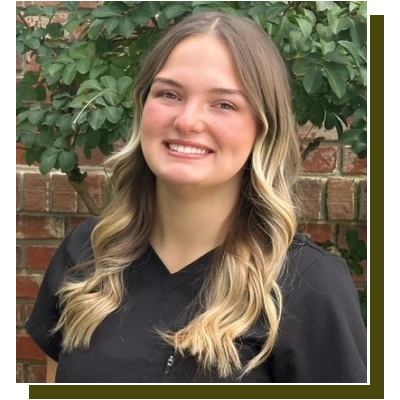 Young woman smiling at camera wearing black shirt against brick and ivy background.