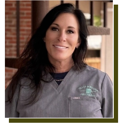 Woman smiling at camera wearing gray Glick & Woods Dentistry shirt in dental office setting.