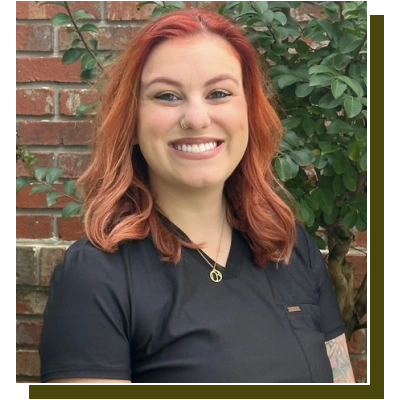 Woman with red hair smiling at camera wearing dark polo shirt against brick wall with ivy.