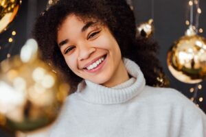 Smiling woman in white sweater against golden holiday decorations and bokeh lights background.