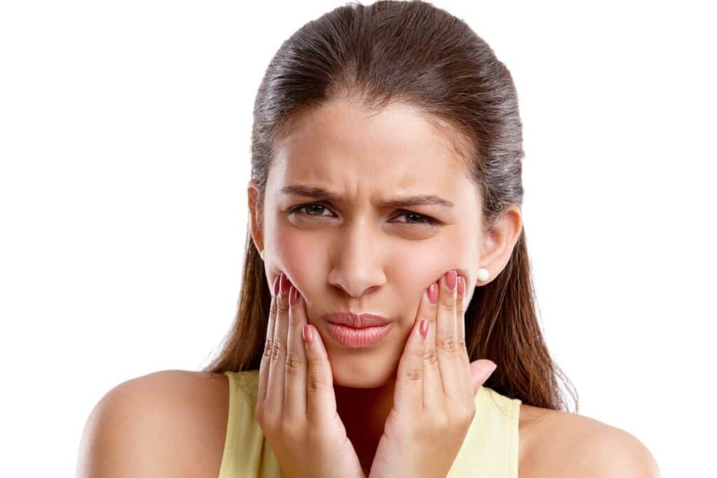 Woman holding her cheeks in pain from tooth sensitivity to cold temperatures.