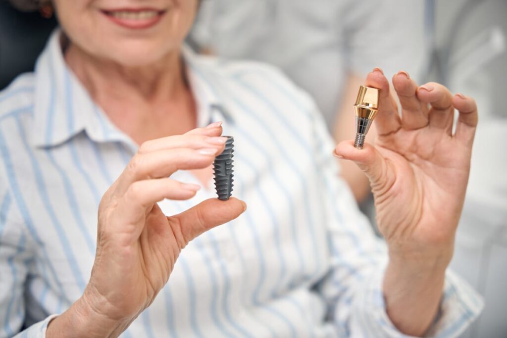 Dentist displaying dental implant components including the screw and crown during a restorative procedure consultation.
